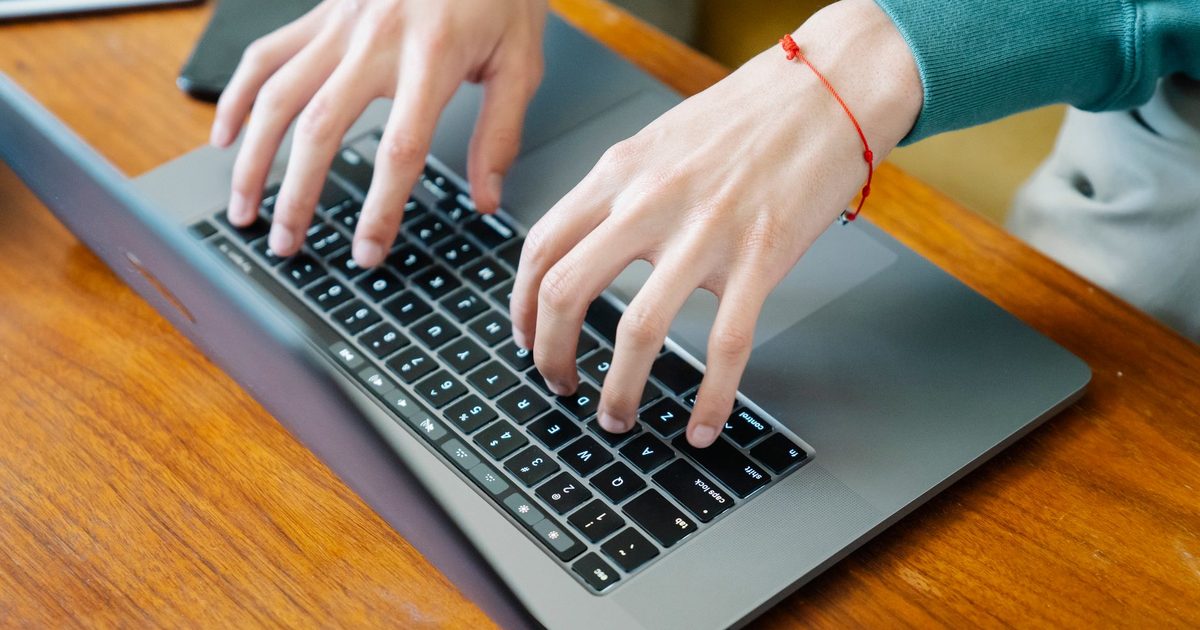 Mani che digitano sulla tastiera di un portatile su un tavolo di legno