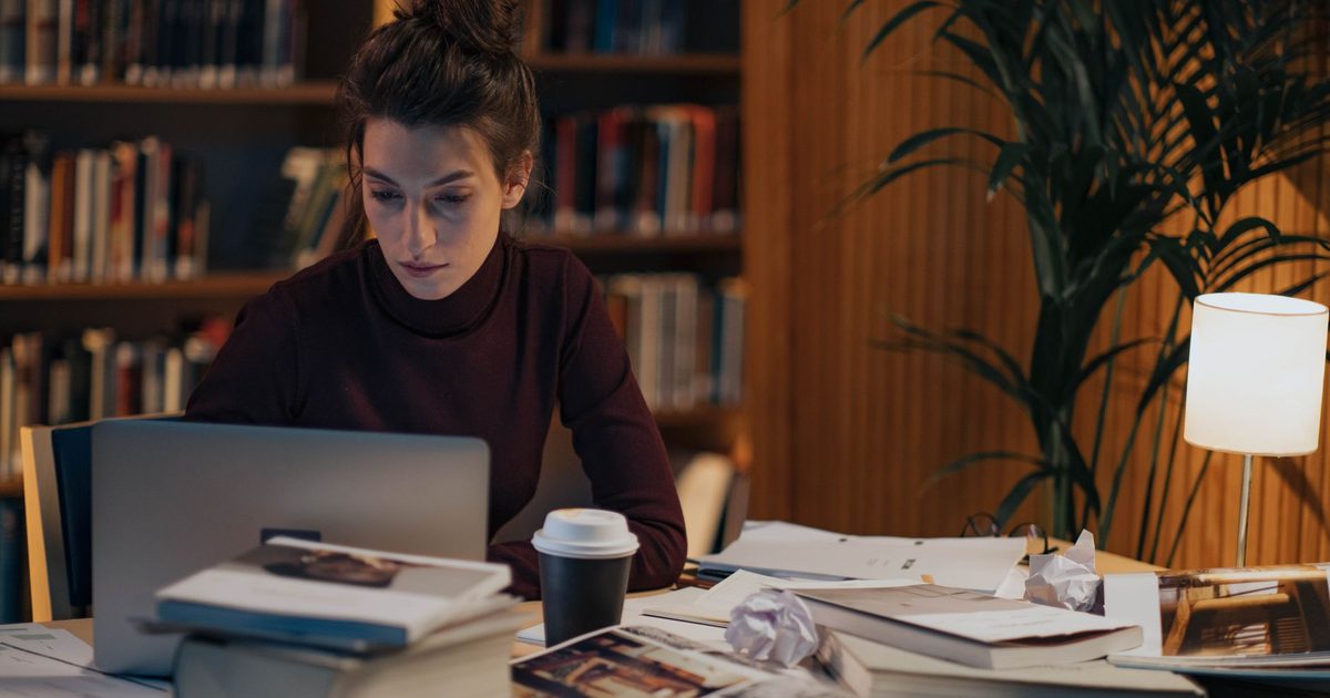 Donna al lavoro a una scrivania coperta di libri aperti e un portatile