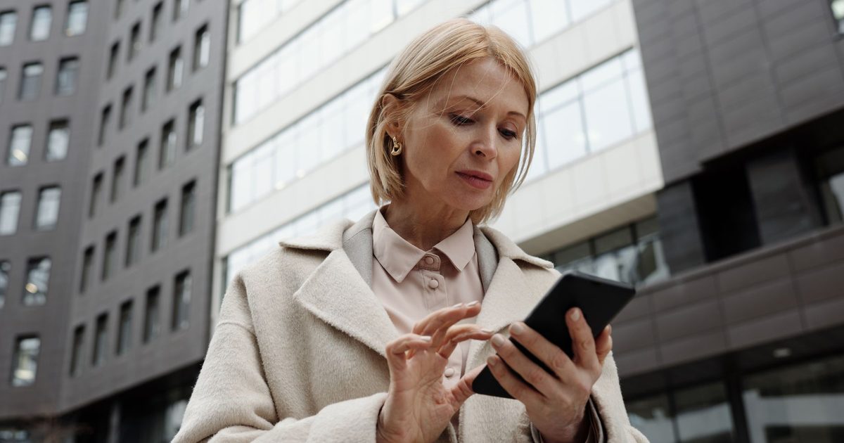 Donna in cappotto che guarda il telefono in una via della città